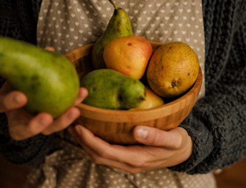 Cozy scene of a person holding a wooden bowl filled with pears and apples.