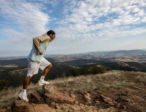 A man jogging on a scenic mountain trail, surrounded by vast landscapes under a clear sky.